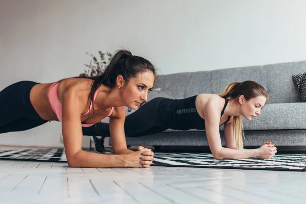 Dos mujeres en forma haciendo ejercicio de tablón en el suelo en casa Entrenamiento de espalda y músculos de prensa, deporte, entrenamiento de fitness — Foto de Stock