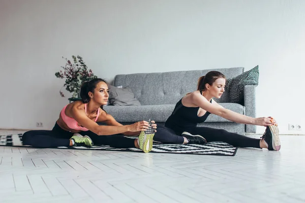 Passa kvinnor gör sträcker sig medan du sitter på golvet hemma — Stockfoto