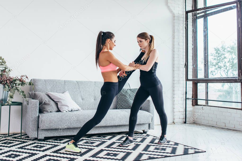 Fit girls preparing legs workout. Leg stretching exercise fitness woman doing warm-up, hamstring muscles stretch standing at home.