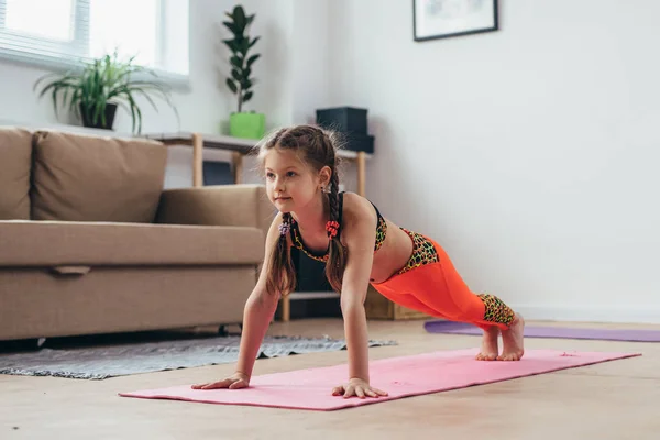 Liten flicka gör plankan träning hemma. — Stockfoto