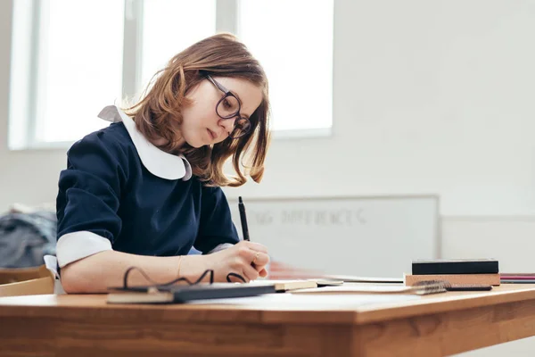 School Girl writes in a notebook sitting at table Classwork, homework Stock Image