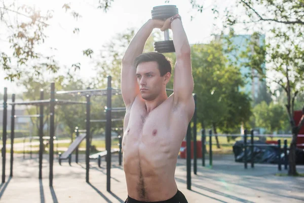 Atleta masculino muscular com braços levantados fazendo exercícios de elevação halteres . — Fotografia de Stock