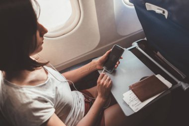 Uçakla seyahat eden kadın. Elinde uçakta oturan bir telefon ile kız.