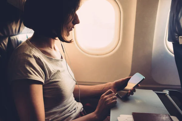 Jonge vrouw op een vliegtuig met een smartphone in haar handen — Stockfoto