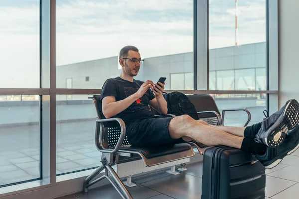 Turista masculino sentado en el banco con equipaje en la sala de espera en el aeropuerto . —  Fotos de Stock