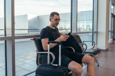 Havaalanında bekleme odasında bagaj ile bankta oturan erkek turist.