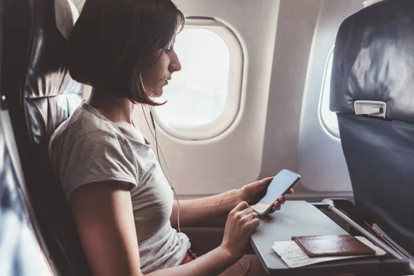 Chica usando un teléfono inteligente mientras vuela en un avión . — Foto de Stock