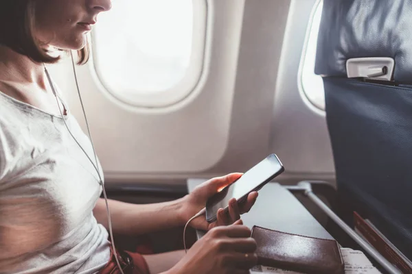 Chica usando un teléfono inteligente mientras vuela en un avión . — Foto de Stock