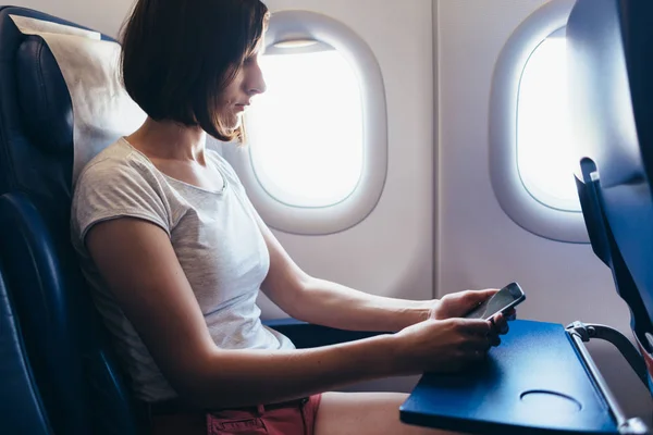 Mujer viajando en avión. Chica con un teléfono en sus manos sentado en el avión . — Foto de Stock