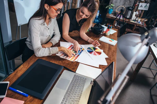 Två kvinnliga Arkitekter arbetar ihop med färg färgrutor som sitter vid skrivbord med laptop, ritplatta i designstudio — Stockfoto