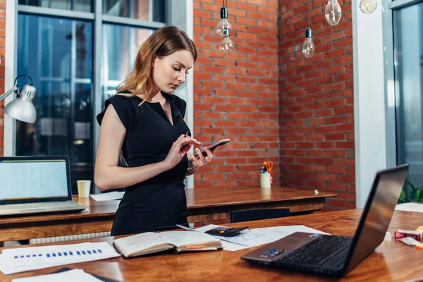 クリエイティブ ・ オフィスの彼女の職場で立っているスマート フォンを使用して働く女性のトップ ビュー — ストック写真