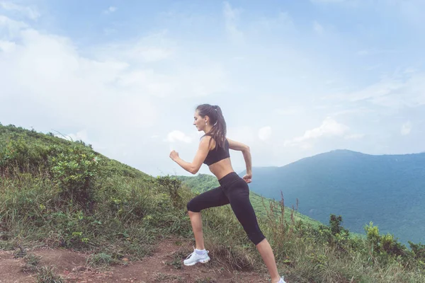 Sidovy av kvinnliga idrottare utbildning, löpning utomhus i gröna berg. Ung kvinna som bär svart sportkläder arbetande ute på sommaren — Stockfoto