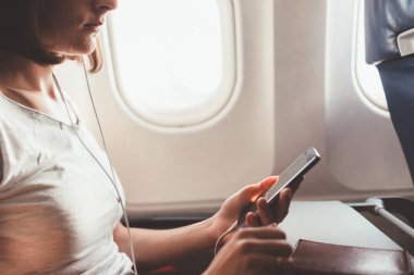 Uçakla seyahat eden kadın. Elinde uçakta oturan bir telefon ile kız.