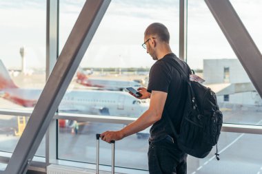 Havaalanında pencerenin yanında duran genç kadın elinde cep telefonuyla