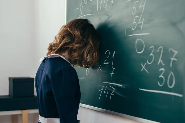 Aluno menina triste tentando resolver um exemplo. Estudante fica com a testa no quadro negro — Fotografia de Stock