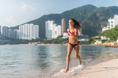 Kadın atlet giyen bikini kumsalda güneş kamera parlıyor ve otel resort hills arka planda çalışan uygun