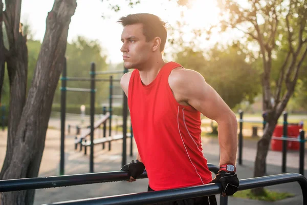 Adatta all'uomo allenamento delle braccia su tuffi barre orizzontali formazione tricipiti e bicipiti facendo flessioni all'aperto . — Foto Stock