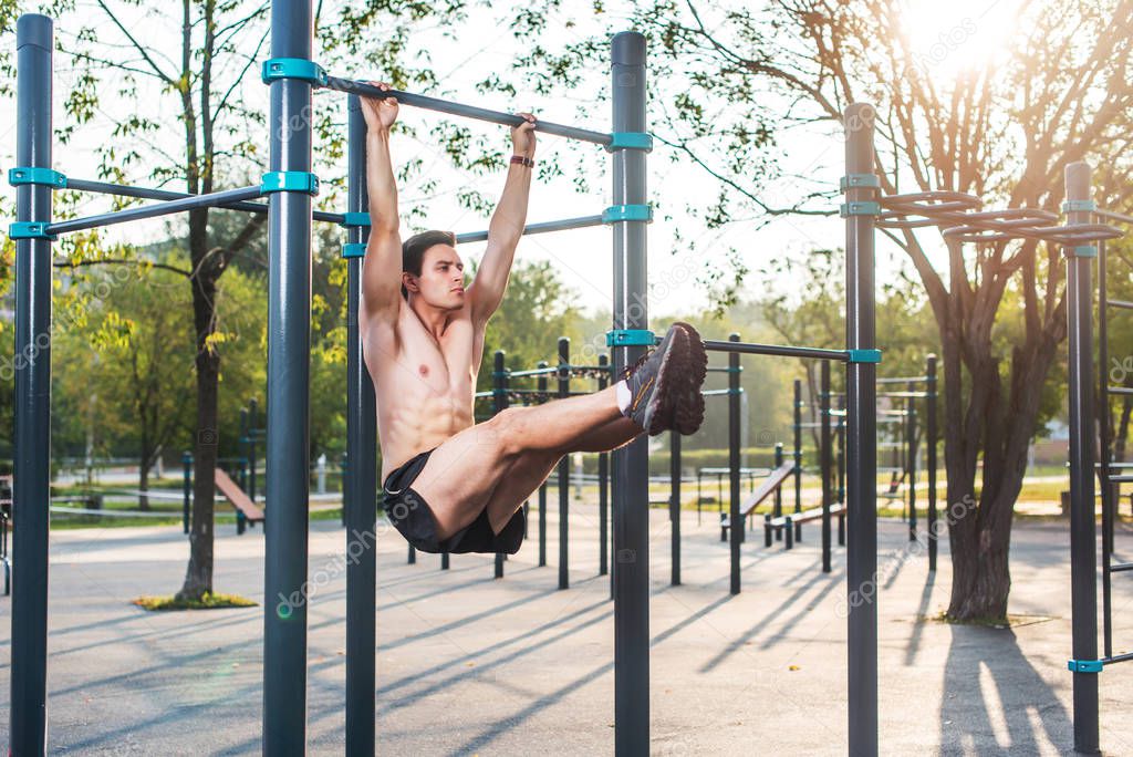 Athlete hanging on fitness station performing legs raises. Core cross training working out abs muscles