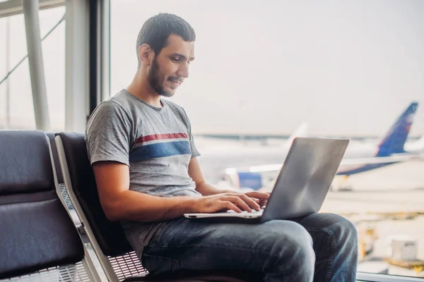 Hombre joven usando el ordenador portátil en la terminal del aeropuerto —  Fotos de Stock