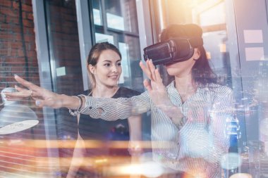 Kadın ofis çalışanları iş yerinde eğleniyor. VR gözlüklü 3D video izliyorlar. Kadın sanal gerçekliği deneyimleyen bir şeye dokunuyor.