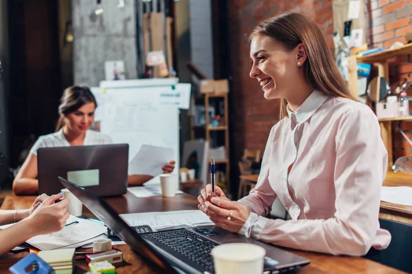 Team av business kvinnor som arbetar med papper använder bärbara datorer sitter vid skrivbord i office — Stockfoto