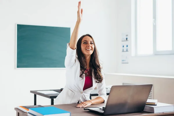 Frau hebt Hand, die wie eine Schülerin am Schreibtisch sitzt. — Stockfoto