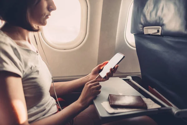 Jonge vrouw op een vliegtuig met een smartphone in haar handen — Stockfoto