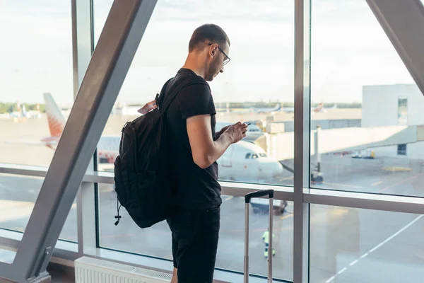 Młoda kobieta stoi w pobliżu okna na lotnisku trzymając telefon komórkowy — Zdjęcie stockowe