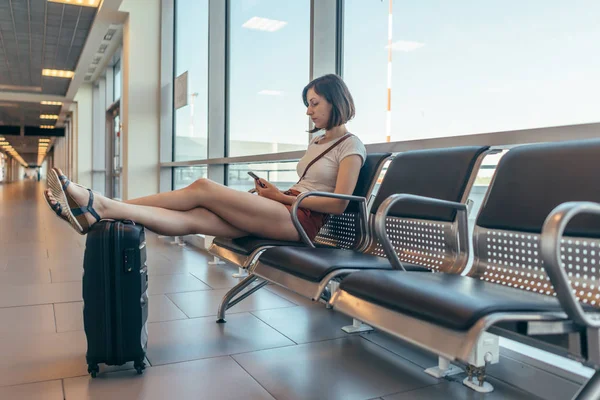 Turista feminino sentado no banco com bagagem em sala de espera no aeroporto . — Fotografia de Stock