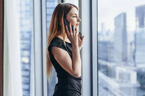 Elegant young female business owner holding documents talking on mobile phone discussing contract conditions standing in office. — Stock Photo, Image