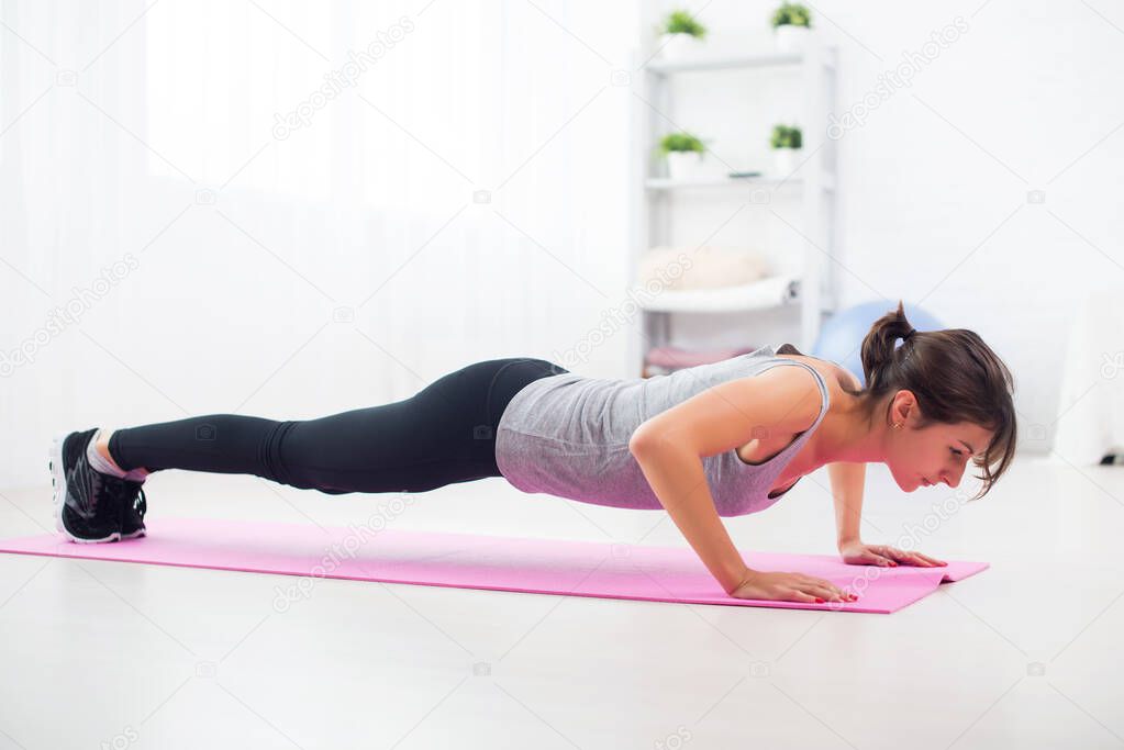 fit woman doing push-ups on the floor in her living room an exercise mat at home