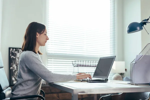 Mujer sentada en su escritorio y usando laptop en la oficina — Foto de Stock