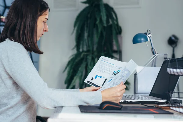 Женщина, работающая за рабочим столом с документами и ноутбуком — стоковое фото
