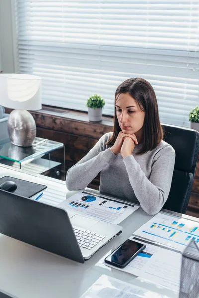 Femme assise devant un écran d'ordinateur portable au bureau avec sa tête appuyée sur ses mains. — Photo