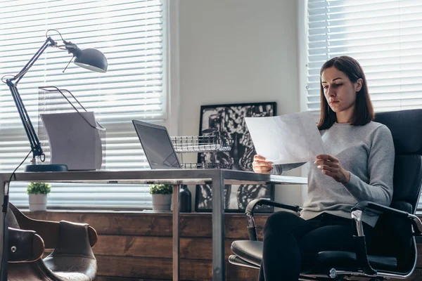 Kvinna arbetar med ett dokument som sitter vid hennes skrivbord — Stockfoto