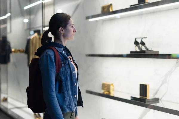 Mujer se para en una ventana boutique y mira los zapatos. — Foto de Stock