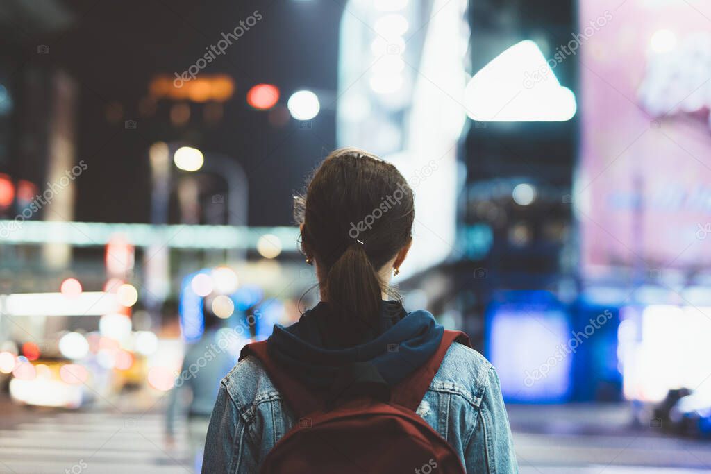 Woman walks through the night city. The view from the back.