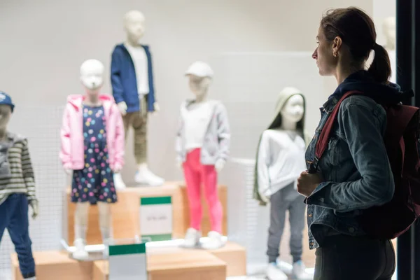 Femme se tient devant le magasin pour enfants et regarde les vêtements sur les mannequins. — Photo