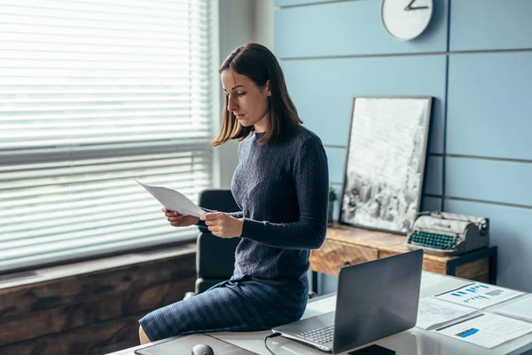 Kvinna på kontoret läser dokument som sitter på ett bord. — Stockfoto