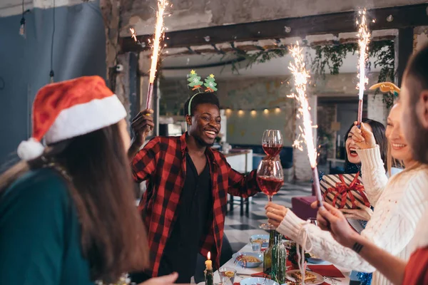 Grupo de pessoas que celebram o Natal ou a véspera de Ano Novo. Amigos brindam com bebidas e jantam juntos. — Fotografia de Stock