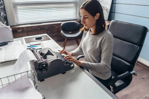 Egy nő az íróasztalánál gépel egy írógépen. — Stock Fotó