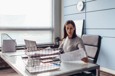 Kadın masaya oturur ve bir belge okur.