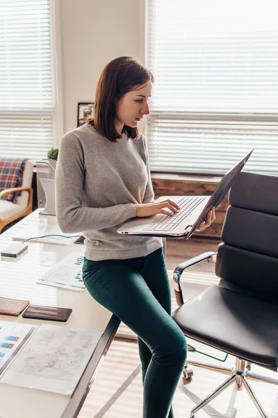 Женщина, стоящая на клавиатуре ноутбука в своем офисе — стоковое фото