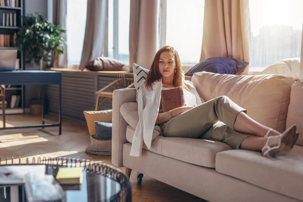 Jeune femme à la maison allongée sur un canapé avec un livre. — Photo