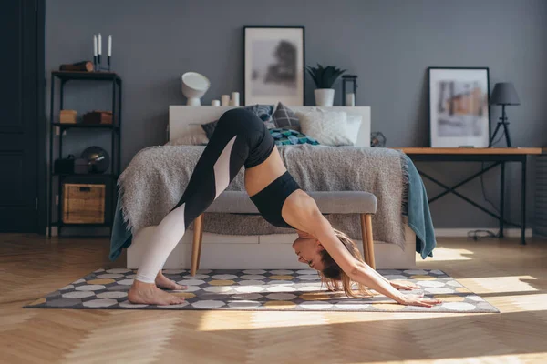 Mulher apta a fazer exercícios de alongamento de manhã em casa. Posição de ioga de cão virada para baixo — Fotografia de Stock