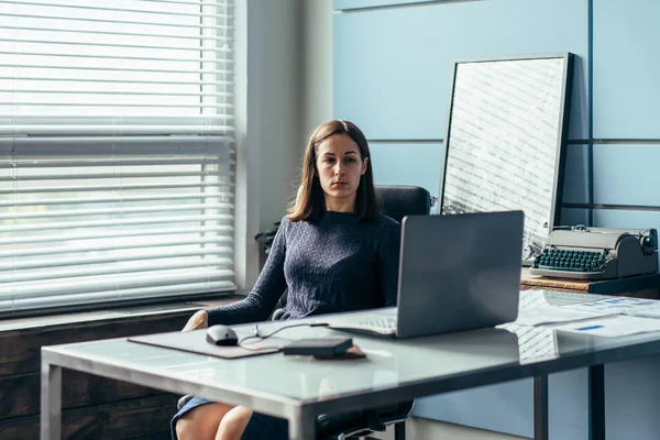 Kvinnan sitter vid bordet och tittar på den bärbara skärmen — Stockfoto