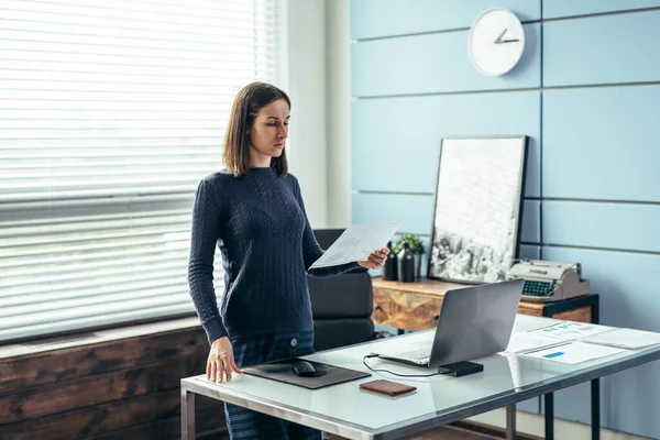 Kvinna står med papper i handen och ser över informationen. — Stockfoto