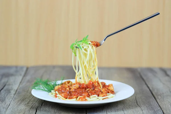 Spaghetti with tomato sauce on silver fork of floating in the white dish on wooden floor,concept of eating good food is health care.