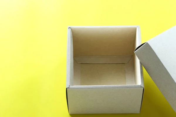 Empty brown paper box rests on a yellow paper floor and have copy space for design in your Christmas work concept.