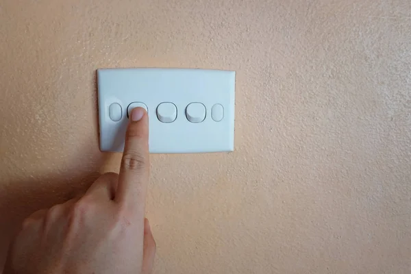 Man\'s hand push button of white switch on orange wall.